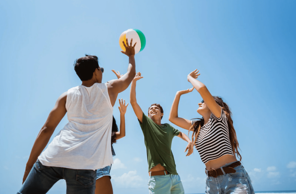 4 teenagers playing with a beach ball against a blue sky