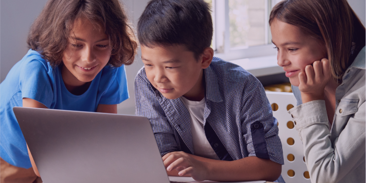 L'image montre trois enfants regardant un ordinateur portable avec une expression intriguée et concentrée.