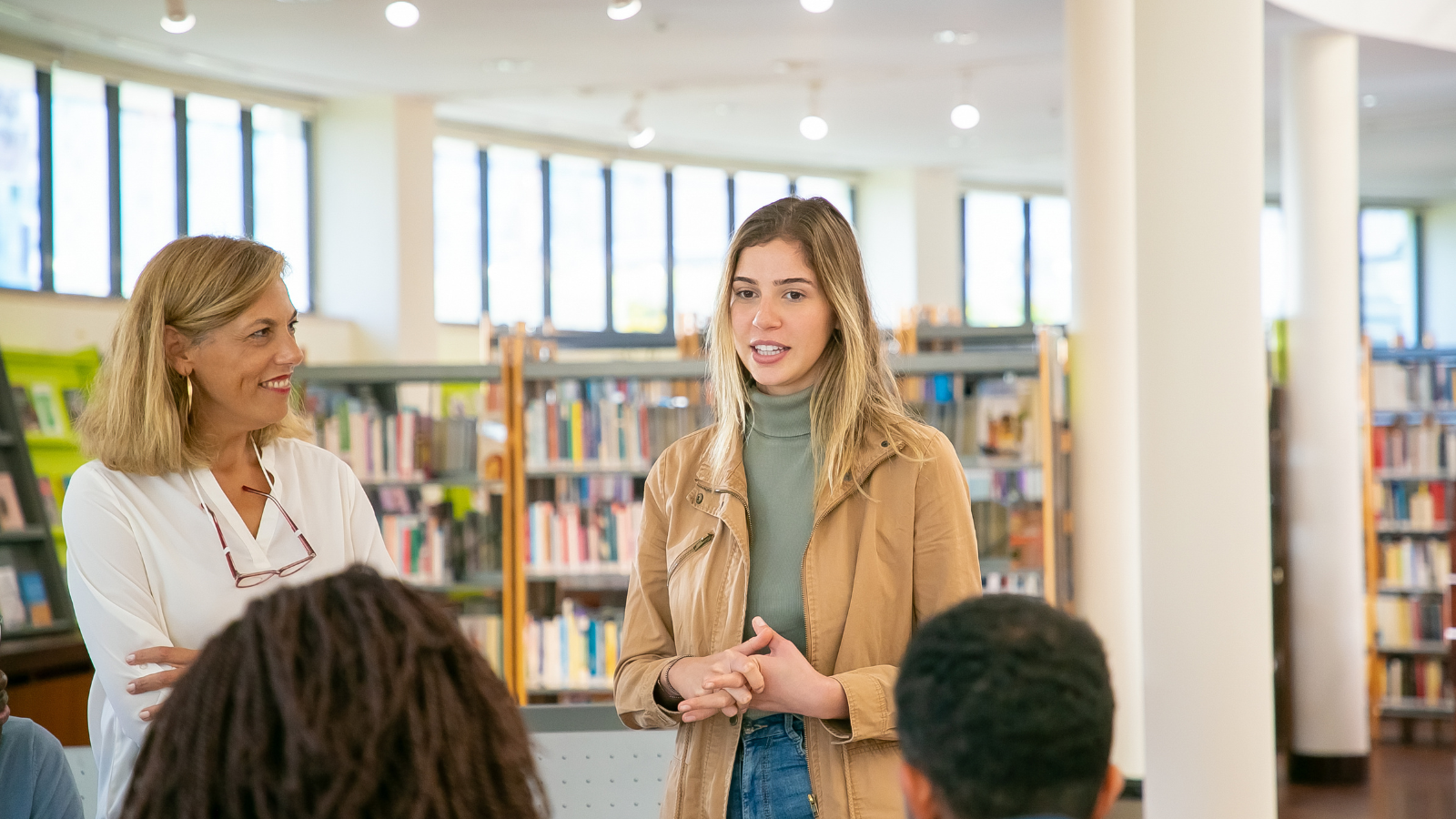 Une femme s'engage avec un groupe de personnes dans une bibliothèque, encourageant la discussion et la collaboration entre eux.