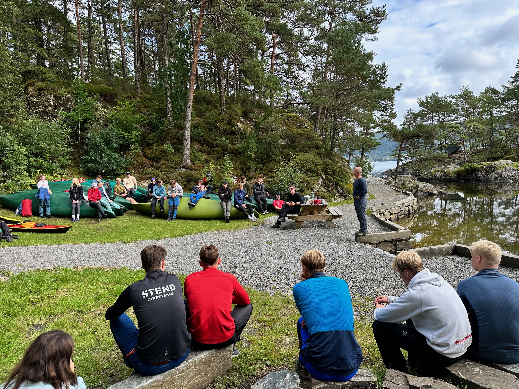 une photo qui montre un groupe d'étudiants en plein air écoutant un professeur