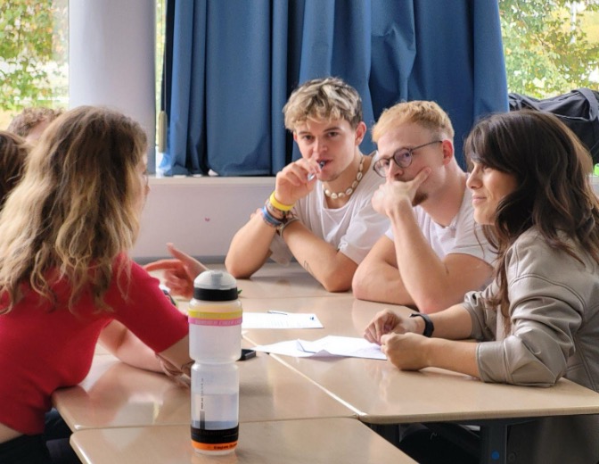 A diverse group of students engaged in conversation while seated around a table, fostering collaboration and discussion.