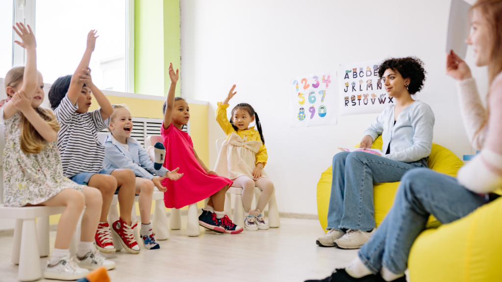 Des enfants assis sur des chaises, levant les mains en signe d'enthousiasme ou de participation.