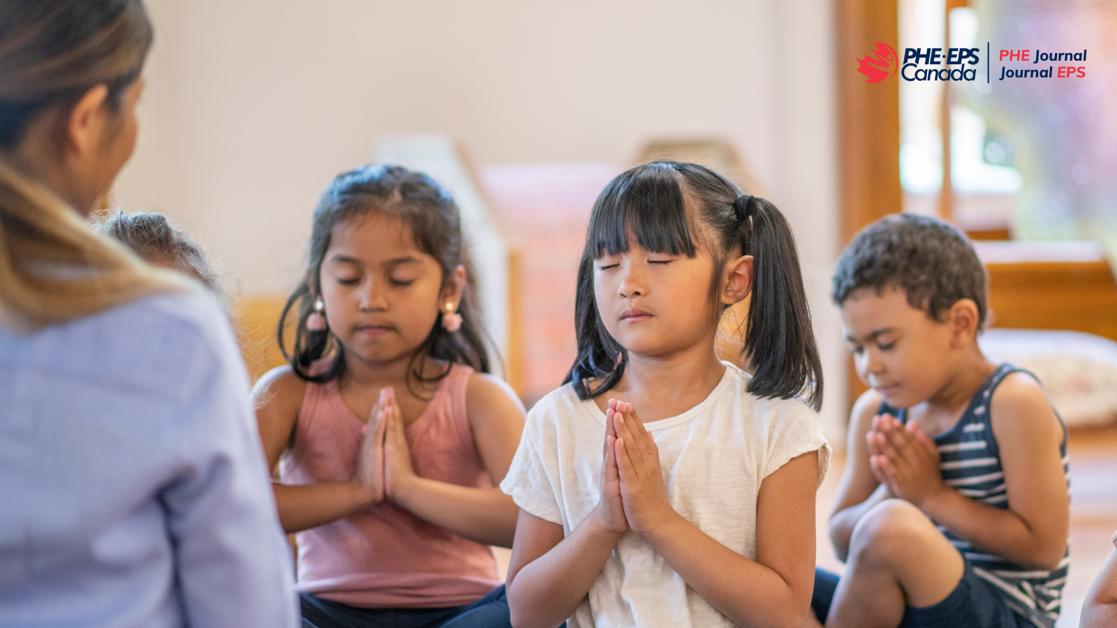 L'image montre trois enfants qui pratiquent la pleine conscience en priant devant leurs professeurs, les yeux fermés.