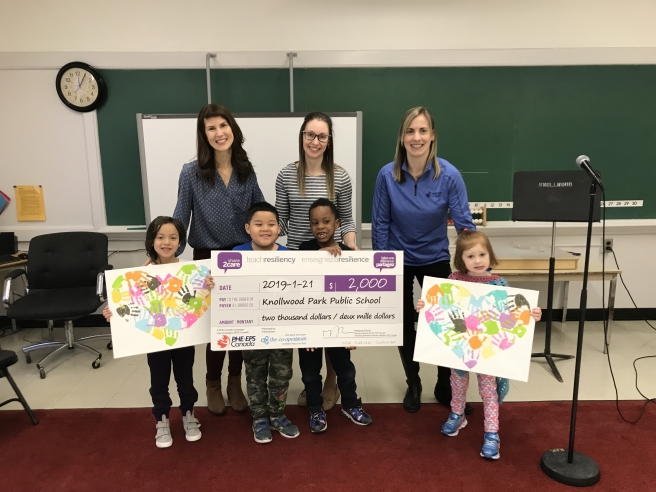 3 adults and 3 children in a classroom holding posters and a cheque for the Share2Care program from PHE Canada
