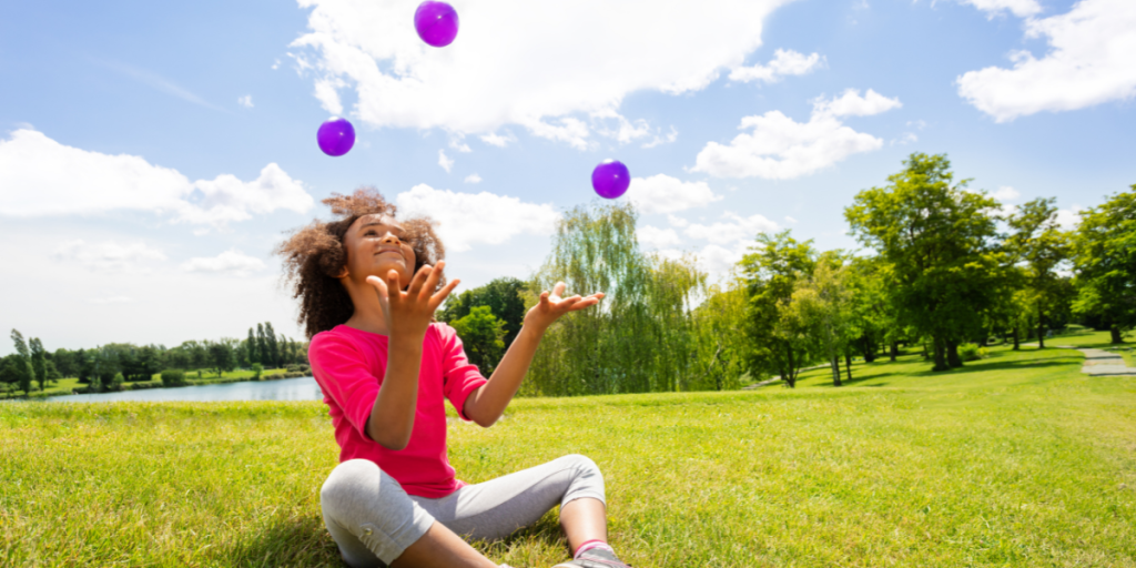 A child is juggling outdoors on a sunny day.