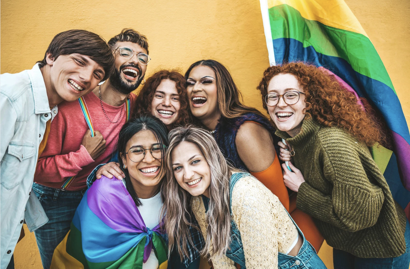a group of youth smiling with a pride flag 
