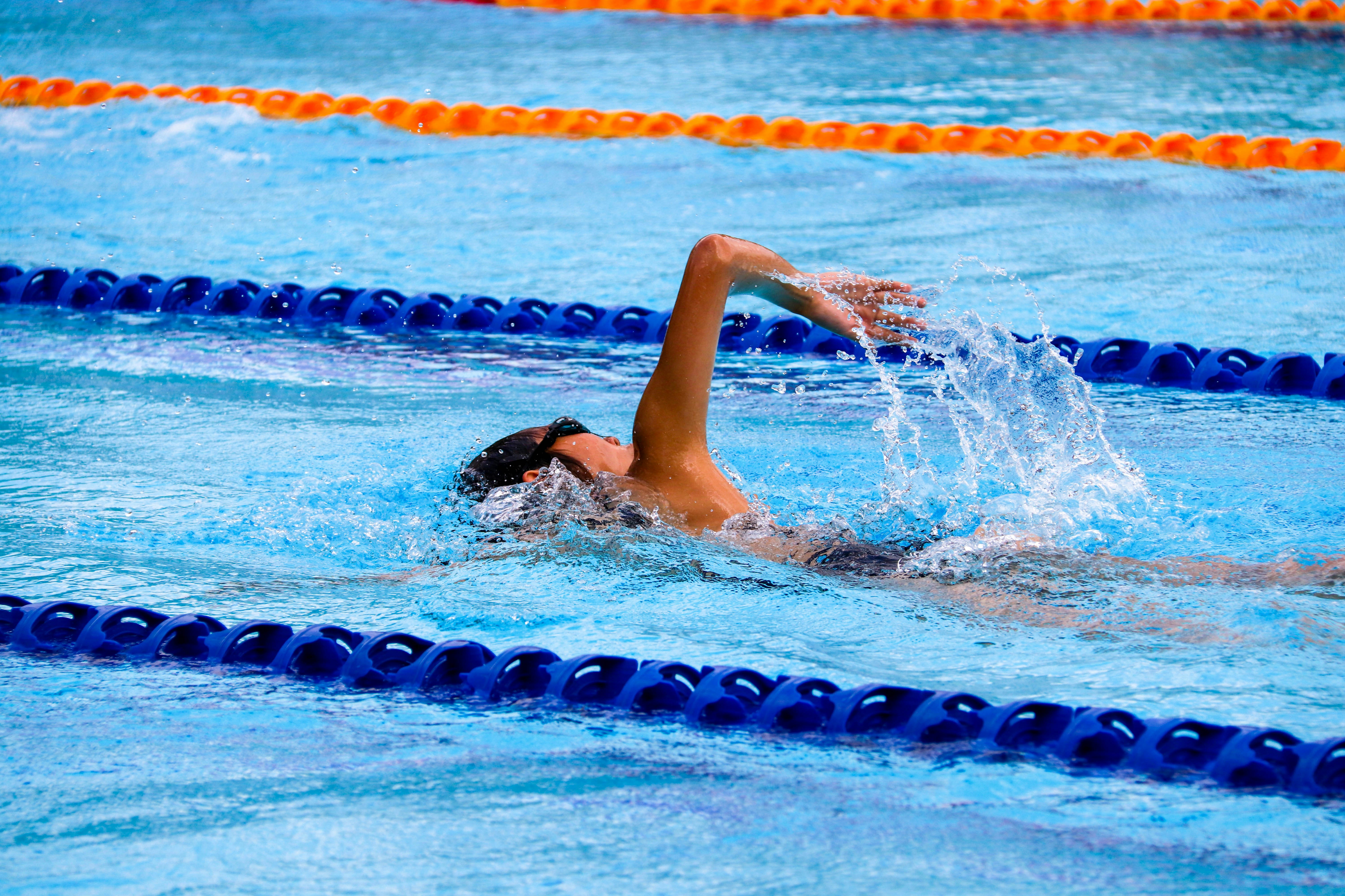 A person swimming in a clear blue pool, creating ripples in the water.