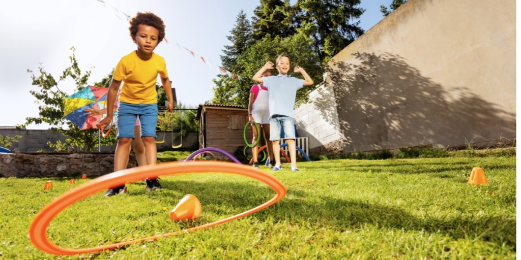 Children play an outdoor game with hoops and cones on a sunny day.