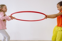 Two children hold a red hoop between them with their hands, smiling.