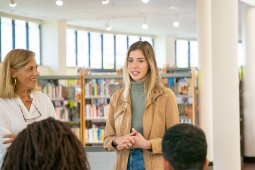 Une femme s'engage avec un groupe de personnes dans une bibliothèque, encourageant la discussion et la collaboration entre eux.