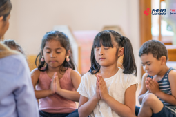L'image montre trois enfants qui pratiquent la pleine conscience en priant devant leurs professeurs, les yeux fermés.