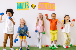 Un groupe d'enfants se tient debout contre un mur blanc, souriant et tenant des balles colorées prêtes à être lancées.