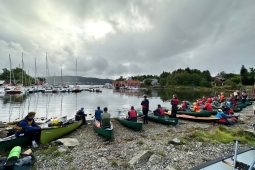 Plusieurs personnes en canoë sont positionnées sur le rivage, s'adonnant à des activités récréatives au bord de l'eau.