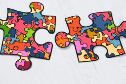 Two colorful puzzle pieces with a mosaic pattern of different shapes and colors on a light wooden background.