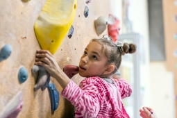 A girl on a climbing wall looking at a yellow climbing hold