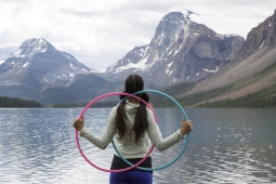 Une jeune fille fait face à une montagne et porte deux cerceaux.