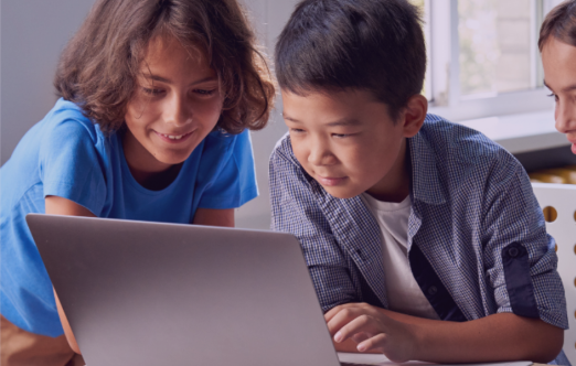 L'image montre trois enfants regardant un ordinateur portable avec une expression intriguée et concentrée.