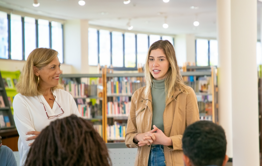 A woman engages with a group of individuals in a library setting, fostering discussion and collaboration among them. - Une femme s'engage avec un groupe de personnes dans une bibliothèque, encourageant la discussion et la collaboration entre eux.