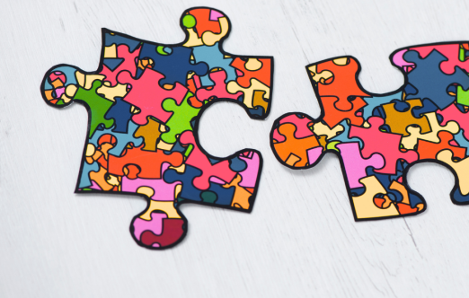 Two colorful puzzle pieces with a mosaic pattern of different shapes and colors on a light wooden background.