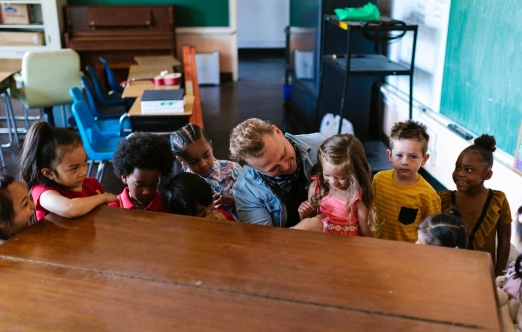 A teacher interacts with children in a bright classroom filled with educational materials and colorful decorations.